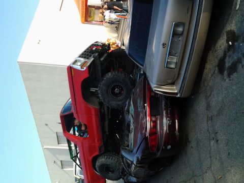 1986 Ford Bronco - A red lifted truck is crushing a red car, with a tan car nearby.