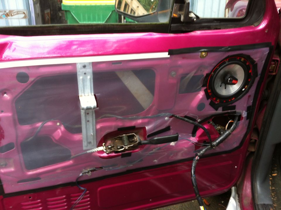 Magenta car door interior with panel removed showing speaker and wiring