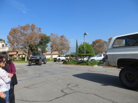 1978 Ford Bronco - Multiple modified trucks and SUVs are gathered in a parking area on a sunny day.