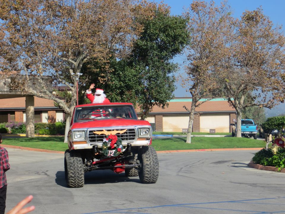 Red lifted 1978 Ford Bronco with Santa driving, waving. Another blue truck is visible in the background