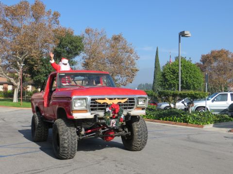 1978 Ford Bronco - A lifted red pickup truck, possibly a 1979 Ford F-Series, drives down a street with Santa in the driver's seat.