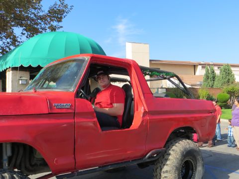 1978 Ford Bronco - A man sits in a red 1978 Ford Bronco, modified for off-road use with large tires and a roll cage.