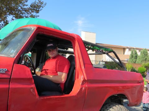 1978 Ford Bronco - A man sits in the driver's seat of a red 1978 Ford Bronco, which features an interior roll cage decorated with tinsel.