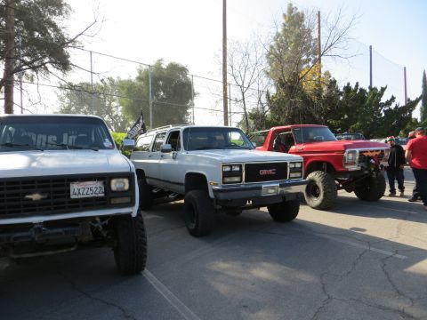 1978 Ford Bronco - Three lifted SUVs are parked in a lot, including a white Chevrolet, a white GMC, and a red Ford.