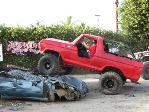 1978 Ford Bronco - A red Ford Bronco is shown crushing a car, with a banner for the 'DESMODR OFFROAD TEAM' in the background.