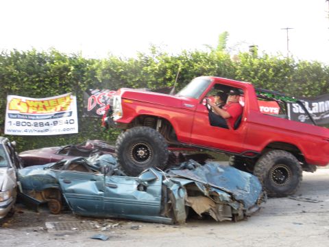 1978 Ford Bronco - A red 1978 Ford Bronco is driven over two heavily damaged cars.