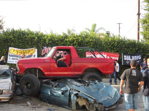 1978 Ford Bronco - A red 1978 Ford Bronco is shown crushing a car, with banners in the background.