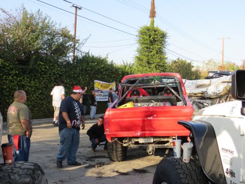 1978 Ford Bronco - A red off-road truck with a roll cage is parked next to other vehicles and people.