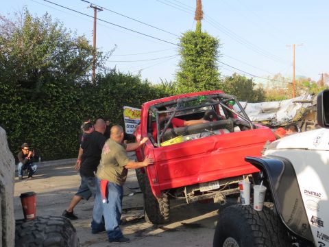 1978 Ford Bronco - A red off-road vehicle with a roll cage is being pushed by several people, with a white Jeep in the foreground.