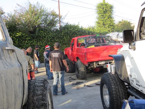 1978 Ford Bronco - A red pickup truck modified for off-roading is parked outdoors with several people around.