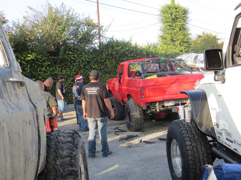 Red pickup truck with roll cage and large tires, parked next to other vehicles