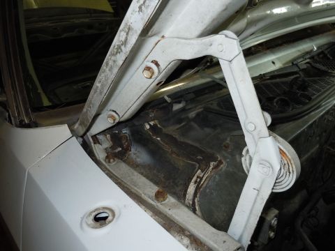 2001 Ford Crown Victoria - The hood hinge and surrounding metal structure of a car, showing signs of rust.