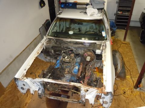 2001 Ford Crown Victoria - A dismantled 2001 Ford Crown Victoria police car sits in a garage, its engine exposed and front end partially disassembled.
