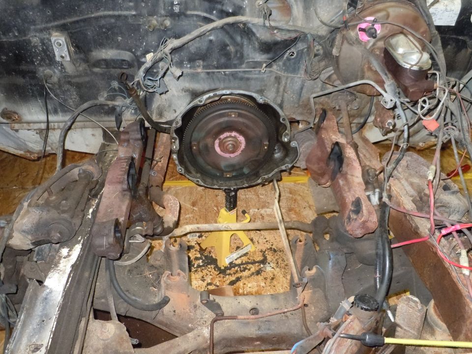 engine and transmission components, including torque converter and exhaust manifold, supported by a yellow jack