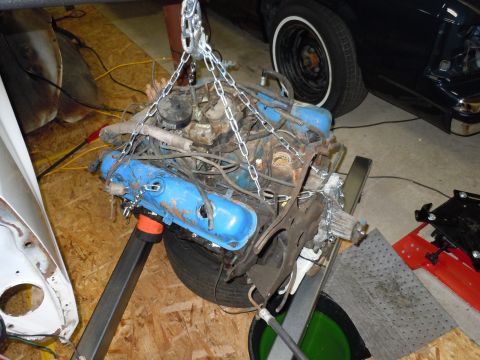2001 Ford Crown Victoria - An engine is being worked on, suspended by chains and resting on a tire.