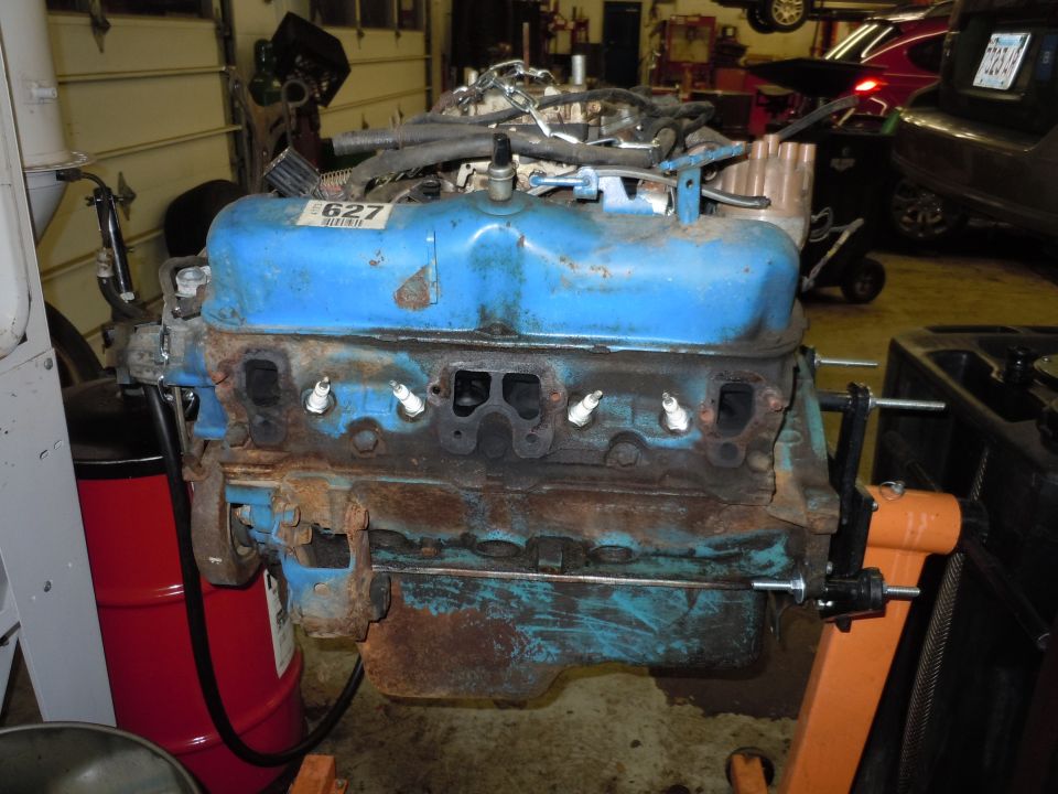 Blue V8 engine block with spark plugs installed, mounted on an orange engine stand