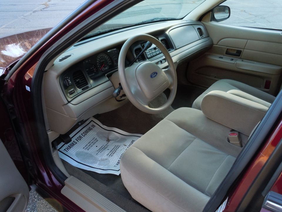 Maroon 2001 Ford Crown Victoria interior with tan seats and dashboard, showing the steering wheel and floor mat