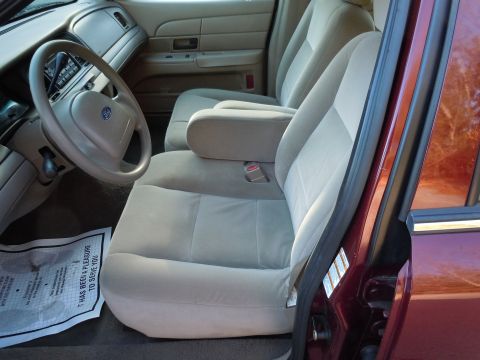 2001 Ford Crown Victoria - The interior of a 2001 Ford Crown Victoria features tan cloth seats and a tan dashboard with a Ford steering wheel emblem.