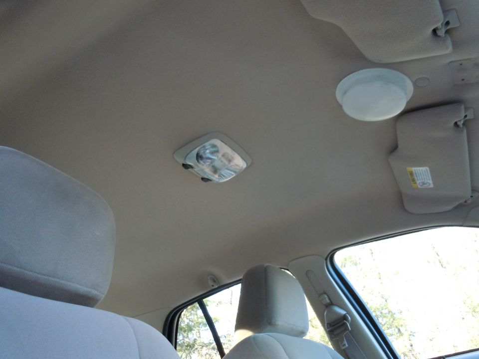 Interior view of car ceiling with two dome lights and sun visors. One visor has a warning label