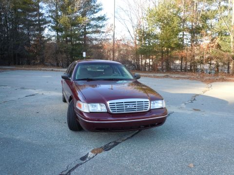 2001 Ford Crown Victoria - A maroon 2001 Ford Crown Victoria is parked on an asphalt lot with trees in the background.