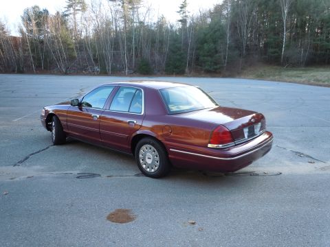 2001 Ford Crown Victoria - A maroon 2001 Ford Crown Victoria sedan is viewed from the rear-right quarter angle in an empty lot.