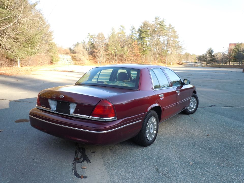 Maroon 2001 Ford Crown Victoria sedan parked on asphalt lot, trees in background