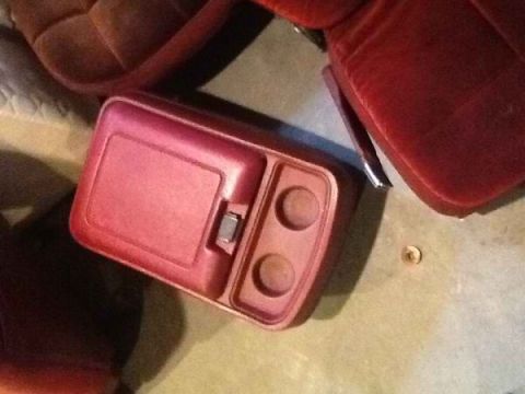 1985 Ford Bronco - A red plastic center console with a flip-top compartment and two cup holders is shown next to a red seat.