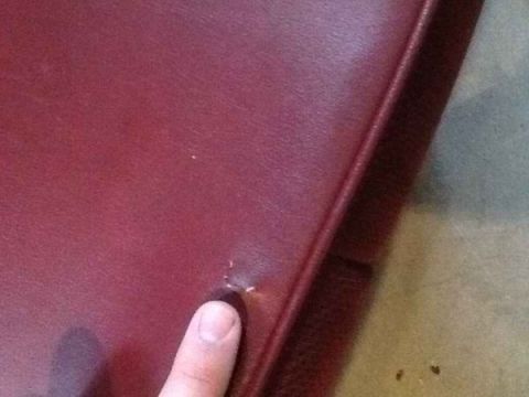 1985 Ford Bronco - Close-up of a red leather seat showing a small tear, with a finger indicating the damage.