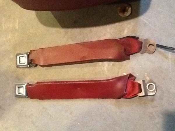 Two red seat belts with metal buckles and mounting points on a textured surface