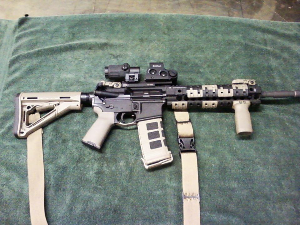 Assault rifle with tan stock and grip, black receiver, and tan camouflage handguard, resting on a green cloth