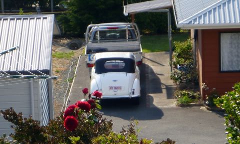 1969 MINI Cooper - A classic white convertible is parked behind a pickup truck in a driveway, with red roses blooming nearby.