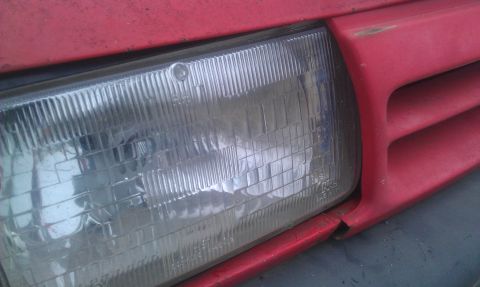 1991 Ford Festiva - Close-up of a red car's front end, showing the headlight and part of the grille.