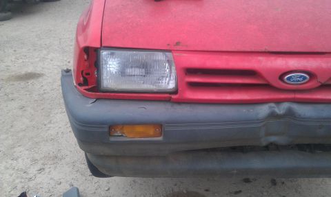 1991 Ford Festiva - Front view of a red car showing a damaged headlight assembly and a dented bumper. The Ford emblem is visible on the grille.