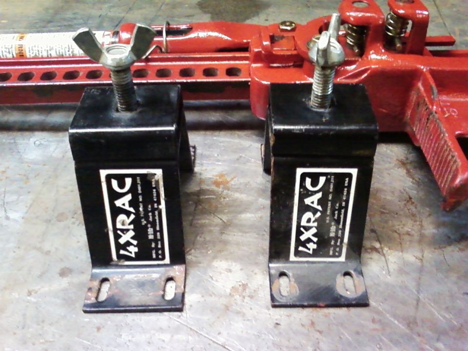 Two black 4XRAC Hi-Lift Jack mounts with wing nuts and a red Hi-Lift Jack in the background