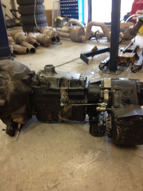 1984 Ford Bronco - A disassembled transmission and transfer case assembly sits on a garage floor, surrounded by other vehicle parts.