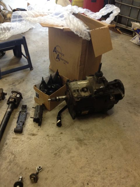 1984 Ford Bronco - Various vehicle transmission and drivetrain components are displayed on a concrete floor, with a box from Advance Adapters in the backgroun…