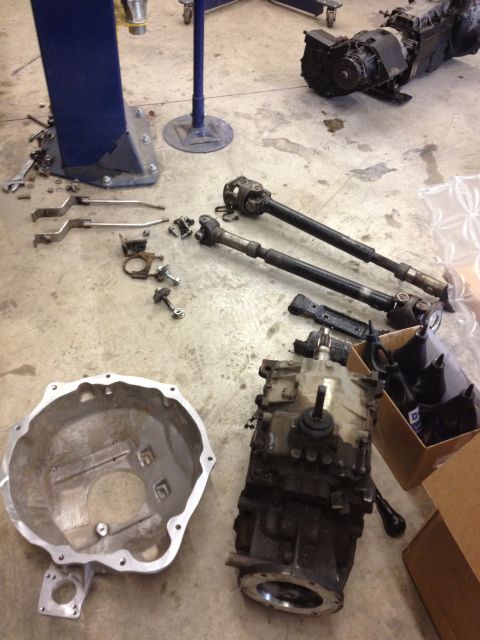 1984 Ford Bronco - Various automotive parts, including a transmission and driveshafts, are disassembled and arranged on a workshop floor.