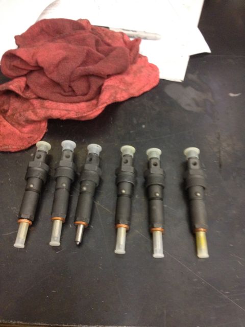 1984 Ford Bronco - A set of six diesel fuel injectors are displayed on a workbench, accompanied by a red shop rag.