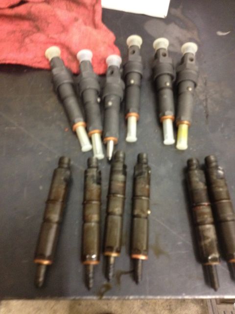 1984 Ford Bronco - Multiple fuel injectors are visible on a workbench, some appear used.