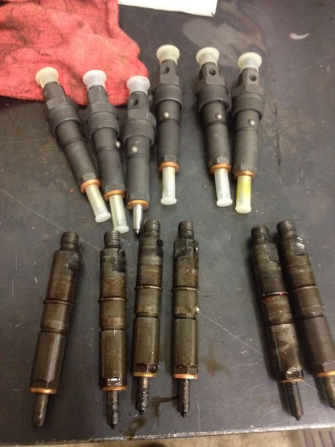 1984 Ford Bronco - A collection of diesel fuel injectors, some appearing cleaner than others, are arranged on a dark surface.