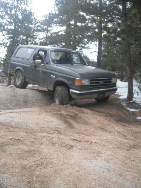 1990 Ford Bronco - This Ford Bronco is navigating a challenging dirt trail with some snow on the ground.