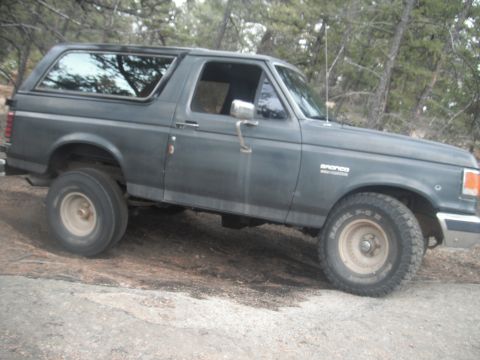 1990 Ford Bronco - This 1990 Ford Bronco is seen off-road on a dirt path, likely in a wooded area.