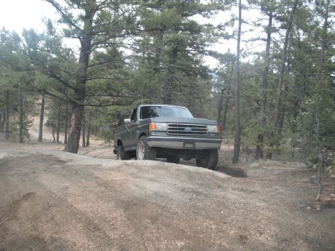 1990 Ford Bronco - A green Ford Bronco drives on a dirt path through a wooded area.