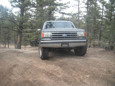 1990 Ford Bronco - Front view of a 1990 Ford Bronco parked on a dirt road in a wooded area.