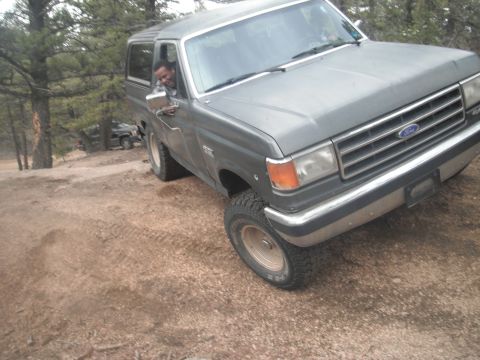 1990 Ford Bronco - A man drives a gray Ford Bronco off-road, with another vehicle visible in the background.