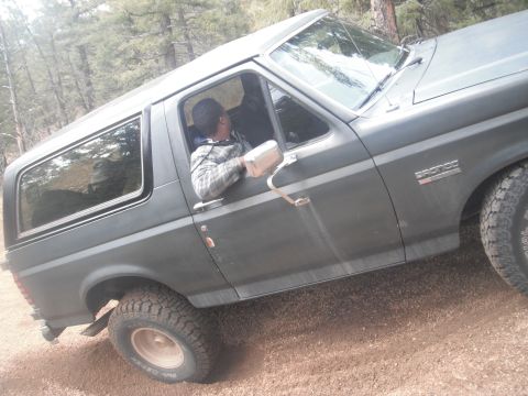 1990 Ford Bronco - This 1990 Ford Bronco is seen off-road in a wooded area, with the driver looking out the window.
