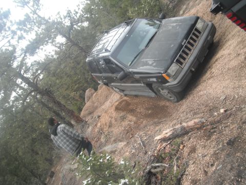 1990 Ford Bronco - A black Jeep Grand Cherokee navigates a rocky trail in a wooded area.