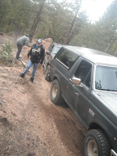 1990 Ford Bronco - Two people are on a dirt trail next to a Ford Bronco, with another vehicle behind it.