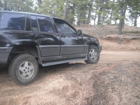 1990 Ford Bronco - A black SUV is parked on a dirt road in a wooded area.