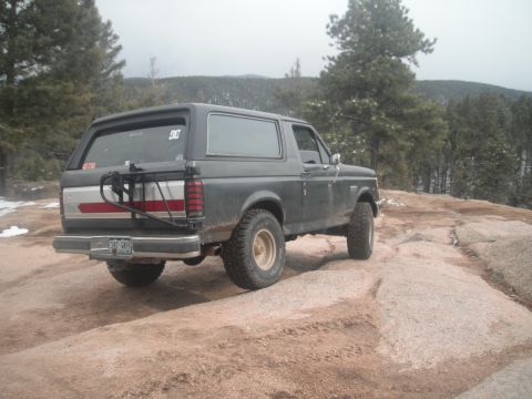 1990 Ford Bronco - This 1990 Ford Bronco is parked on a rocky incline, with a wooded area and mountains visible in the distance.